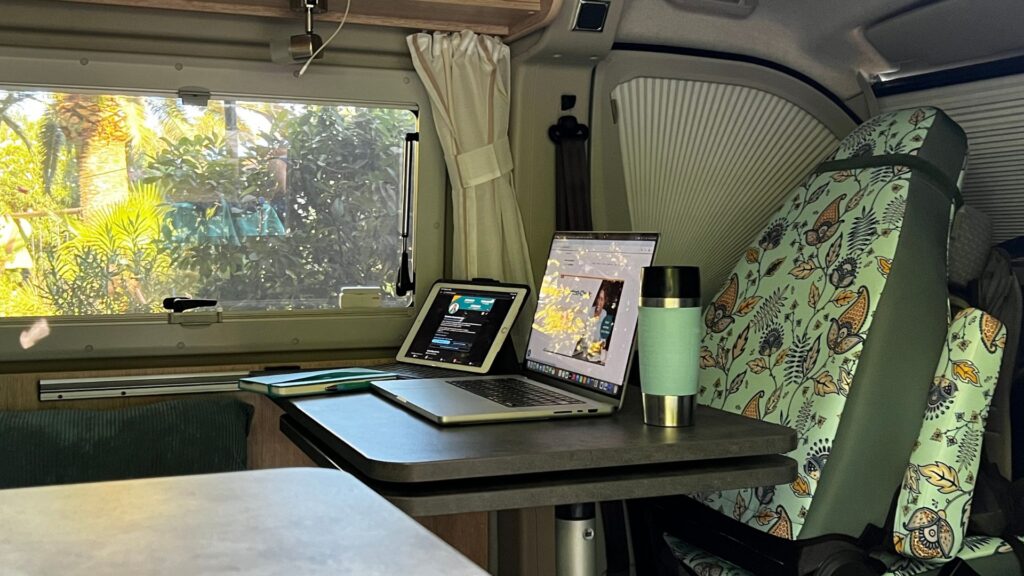 Arbeiten im Camper: Mobiler Arbeitsplatz einer Solounternehmerin mit Laptop, Tablet und Notizbuch während einer Workation.